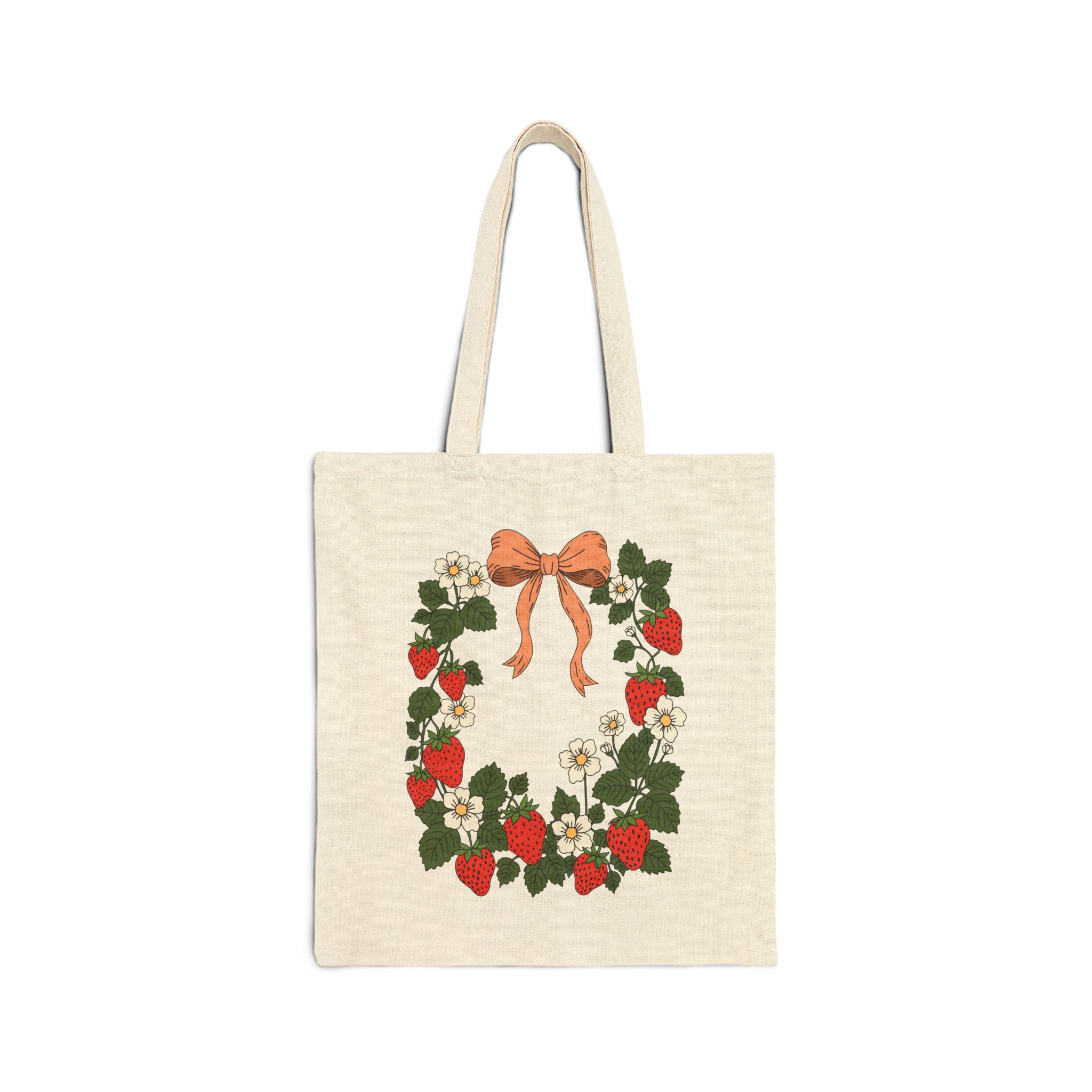 Cotton canvas tote bag featuring strawberry wreath artwork with red strawberries, white flowers, green leaves, leafy vines, and a bow in cottage garden style.