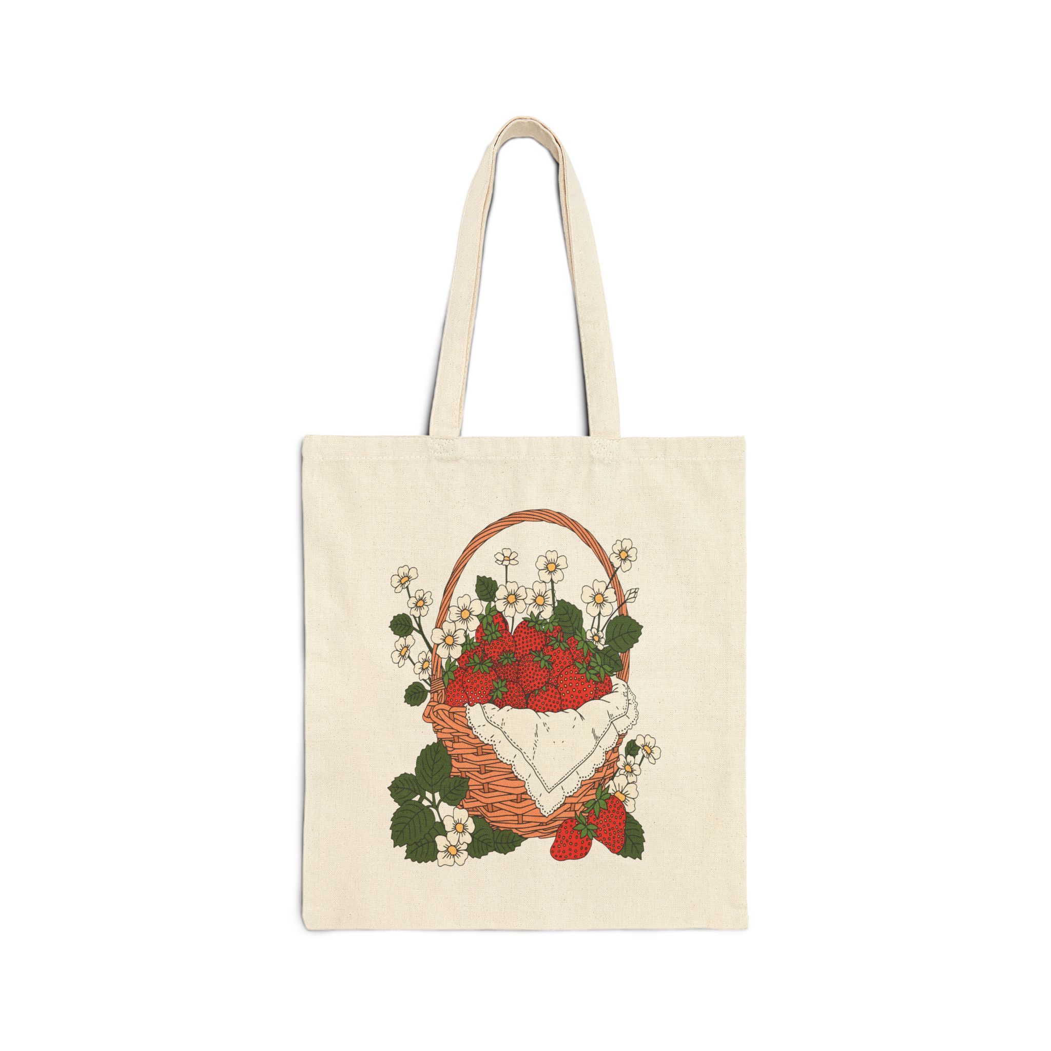 Cotton canvas tote bag featuring strawberry basket artwork with illustrated red berries, white flowers, green leaves, and cottage garden details.